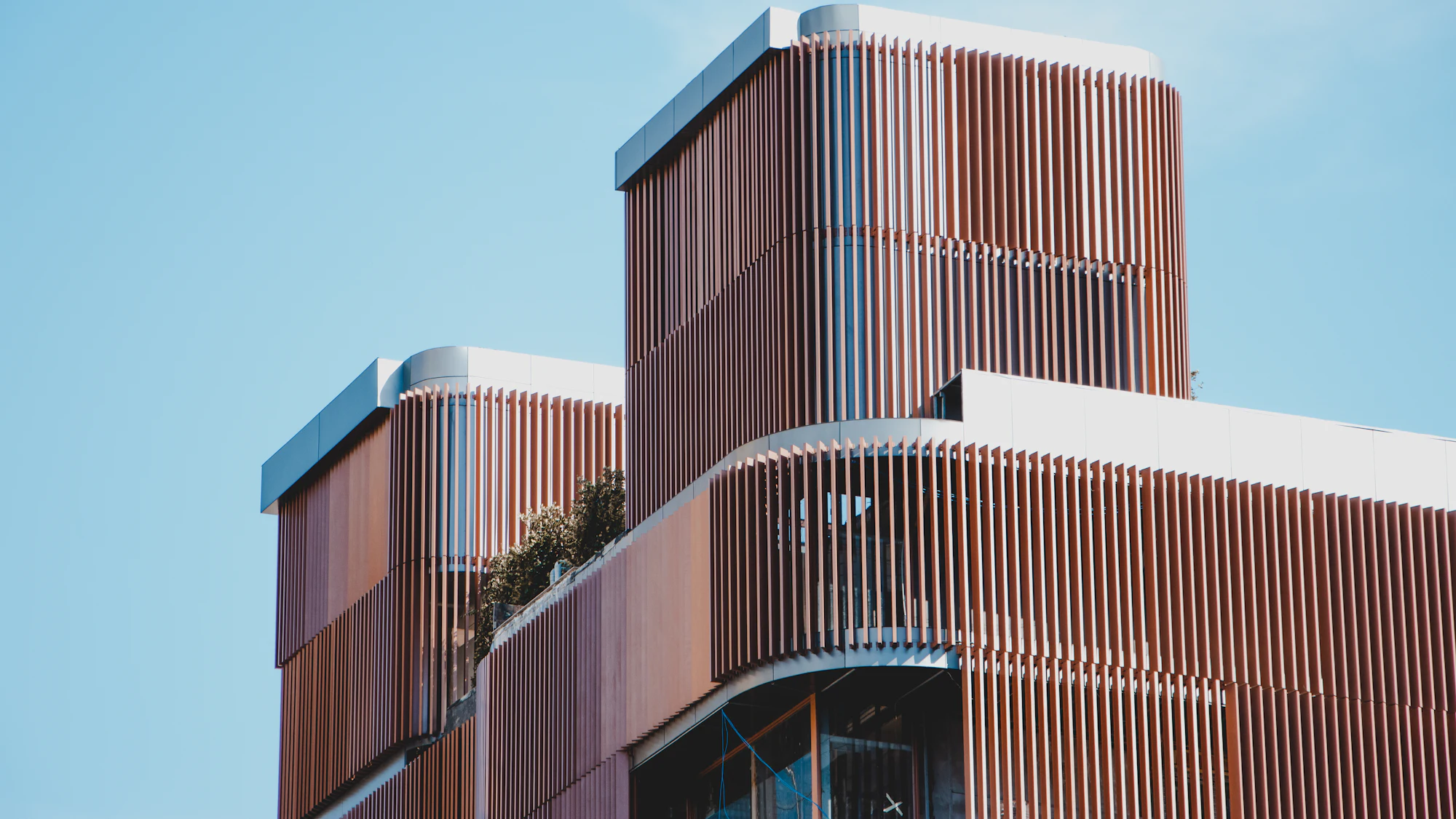 Concept: timber fins wrapping the curved upper floors of an office tower against a clear sky